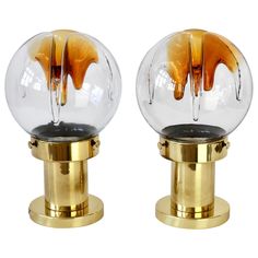 two clear glass balls with gold bases on white background, one has an orange liquid flowing out of it