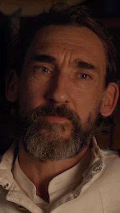 a man with a beard and white shirt looking at the camera in a dark room