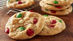 two cookies with m & m's puddings are on a wooden table next to a cooling rack