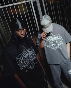 two young men standing next to each other in front of a metal fence and gate