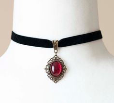 Indulge in the dark elegance of the Victorian era with this enchanting choker, crafted from luxurious black velvet ribbon and adorned with an antique bronze filigree pendant housing a blood-red glass cabochon. Perfect for enhancing your Gothic vampire aesthetic, this necklace is a timeless accessory. Key Features: Material: Black velvet ribbon and antique bronze filigree pendant with blood-red glass cabochon Choker Length: 12 inches (30.5cm), 0.4 inches (10mm) wide Pendant Size: Approximately 1 Adjustable Vampire Style Choker As Gift, Adjustable Vampire Style Choker For Gift, Vampire Style Adjustable Choker As Gift, Gothic Pendant Choker For Party, Antique Adjustable Choker As Gift, Adjustable Gothic Necklace For Formal Occasion, Steampunk Choker Jewelry Gift, Gothic Pendant Choker As A Gift, Gothic Adjustable Choker For Formal Occasions