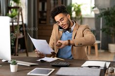 a man sitting at a desk with papers in front of him and looking at his computer screen