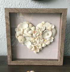 a heart made out of seashells is displayed in a shadow box on a table