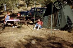 two children sitting in front of a tent with a picnic table and chairs next to it