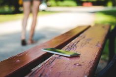 a cell phone sitting on top of a wooden bench next to a woman's legs