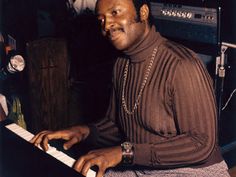 a man sitting at a keyboard with his hands on the keys and wearing a turtle neck sweater