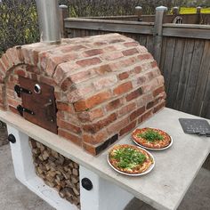 two pizzas sitting on top of a table next to a brick oven and grill