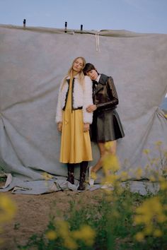 two women standing next to each other in front of a tarp with yellow flowers