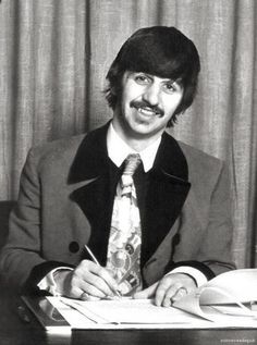 a man in a suit and tie sitting at a desk writing on a piece of paper