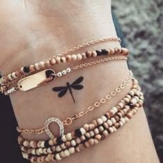 a woman's arm with three bracelets on it and a dragonfly tattoo