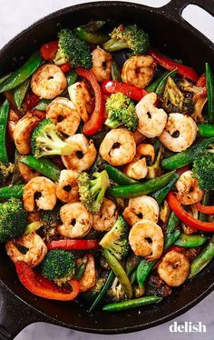 a skillet filled with shrimp, broccoli and peppers