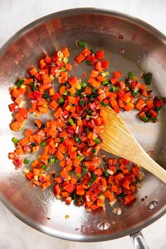 chopped carrots and green onions being cooked in a frying pan with a wooden spoon