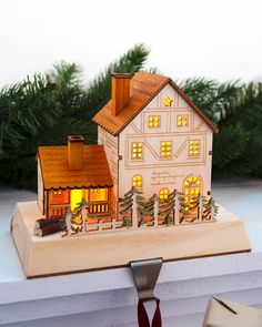 a small wooden house is lit up with christmas lights on the windowsill and trees in the background