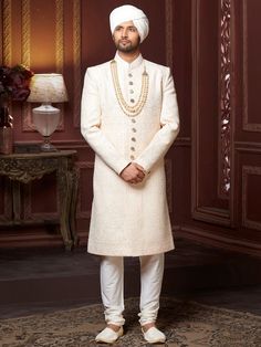 a man in a white sherve with pearls on his neck and pants, standing next to a table