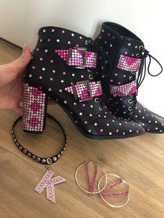 a pair of black boots with pink and white sequins on them are being held by a woman's hand