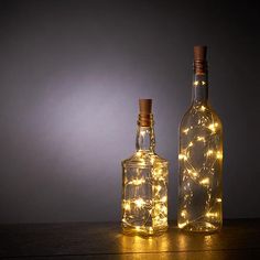 two bottles with lights in them sitting on a table next to each other and one bottle is empty