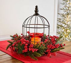 a birdcage filled with holly and candles on top of a red table cloth