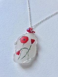 a white necklace with red flowers on it and a silver chain hanging from the neck