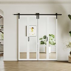 an open room with white walls and wooden flooring, two plants in vases on either side of the glass doors