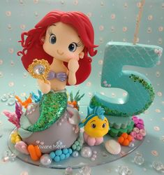 there is a little mermaid sitting on top of the number five cake with bubbles around it