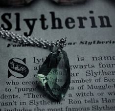 a green necklace sitting on top of an old newspaper with the word slytherin written below it