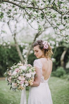 a woman in a wedding dress holding a bridal bouquet under a tree with white and pink flowers