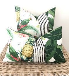 two pillows with pineapples and palm leaves on them sitting on a wicker chair