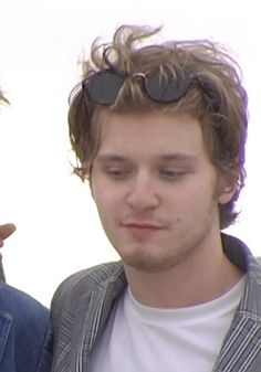 two young men standing next to each other looking at their cell phones, one with his eyes closed