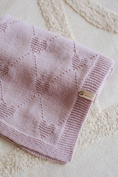 a pink knitted blanket laying on top of a white bed next to a pillow