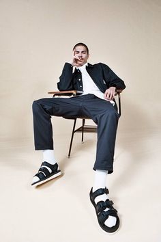 a man sitting in a chair with his legs crossed and wearing black shoes, white shirt and blue pants