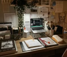 an office desk with a laptop, books and papers on it in front of a plant