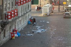 trash on the ground next to a building and people walking down the street in front of it