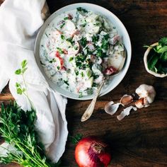 a bowl of food on top of a wooden table next to some vegetables and herbs