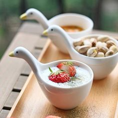 two white bowls filled with food on top of a wooden table next to fruit and nuts