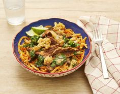 a blue bowl filled with noodles and meat on top of a table next to a glass of water