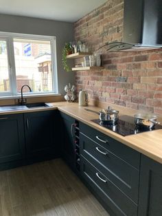 a kitchen with black cabinets and wooden counter tops next to a brick wall that has a window in it