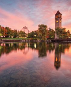 the clock tower is reflected in the still water at sunset, with other buildings and trees behind it