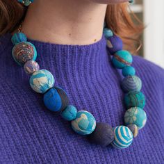 a woman wearing a purple sweater and blue necklace with beads on it's neck