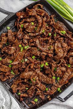 a tray filled with meat and green onions on top of a white table cloth next to some celery