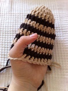 a hand holding a crocheted hat on top of a white bed sheet with black and brown stripes