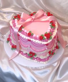 a heart shaped cake with pink frosting and red roses on top, sitting on a white table cloth