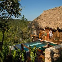 an outdoor hot tub in front of a thatched hut with a woman standing on it