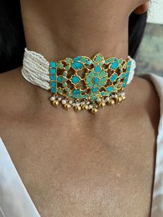 Handcrafted by fine jewelry artisans, this stunning choker necklace set is the perfect accessory for destination weddings and special occasions. Made of 925 silver, the choker features striking turquoise stones and delicate freshwater pearls, adorned with elegant golden ball hangings that add a touch of luxury. This timeless piece is designed to make you stand out. Necklace Weight: 56 grams Materials: 925 Silver, Turquoise, Freshwater Pearls, Golden Ball Hangings Closure Type: Hook closure and is adjustable. The set includes beautifully matching earrings that complete the look. Earrings Weight: 12 grams per pair. Earrings Dimensions: Length is 2 cm and width is 2 cm. Closure Type: Push Back Closure Add this one-of-a-kind, radiant choker set to your collection and let its unique design make Turquoise Fusion Jewelry For Wedding, Traditional Turquoise Choker Jewelry, Turquoise Beaded Fusion Jewelry, Elegant Handmade Turquoise Choker, Handmade Elegant Turquoise Choker, Elegant Turquoise Jewelry For Celebration, Traditional Turquoise Choker Necklace, Festive Turquoise Gemstone Jewelry, Turquoise Beaded Jewelry For Celebration