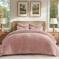 a bed with pink comforter and two pictures on the wall in front of it