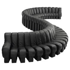 the curved couch is made out of black leather and has multiple sections that are connected to each other