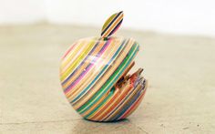 an apple that has been made out of strips of colored paper and is sitting on the ground