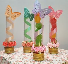 three vases with flowers and butterflies in them sitting on a tablecloth covered table