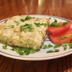 a white plate topped with meat covered in gravy next to a slice of tomato