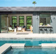 an outdoor kitchen next to a pool with chairs and tables on the patio near it