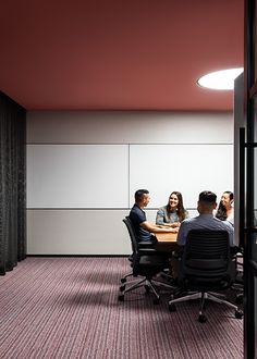 three people sitting at a table in an office setting with pink walls and carpeting